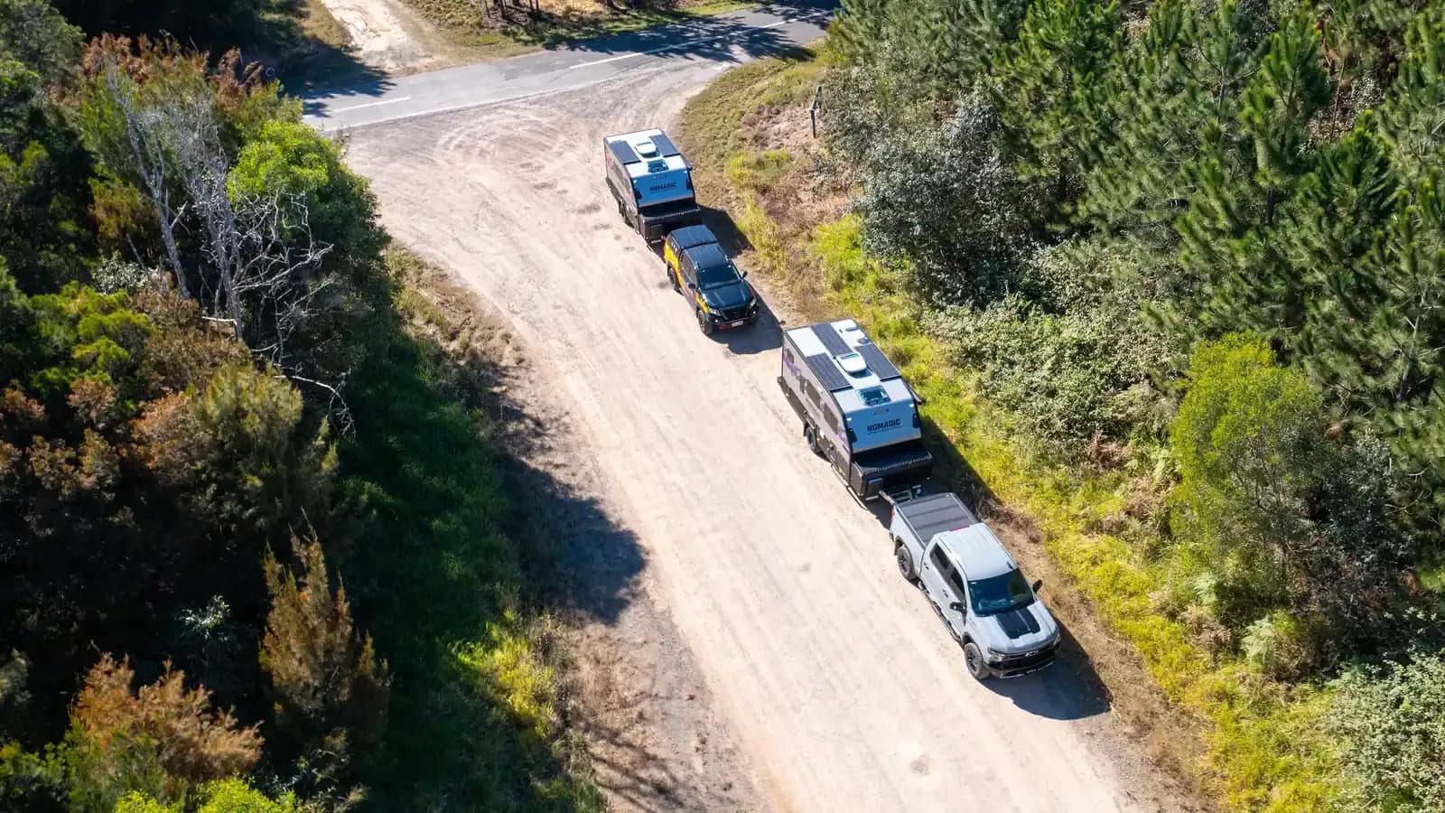 Two Nomadic off-road campers towed by four-wheel drives along a forest dirt road, aerial view