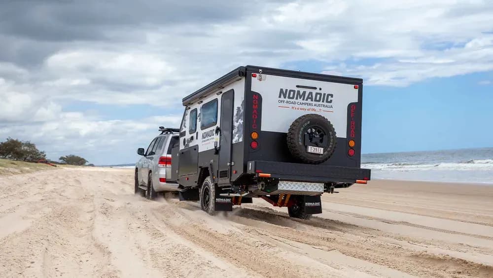 Nomadic off-road camper towed along a beach behind a four-wheel drive