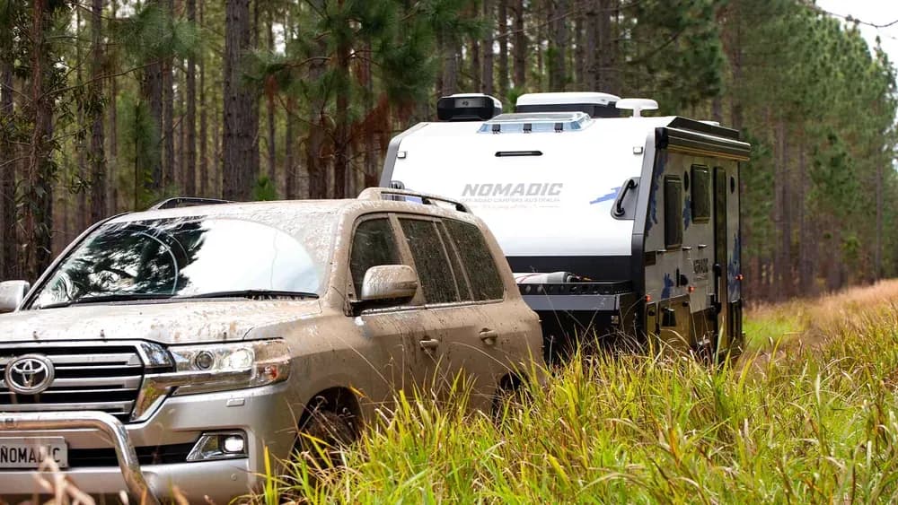 Mud-splattered tow rig parked beside a Nomadic pop-top camper in a pine forest