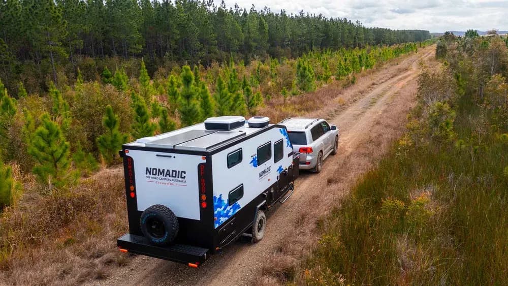 Nomadic off-road camper and tow rig on a dirt track through a pine forest